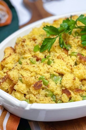 Baked cornbread dressing (cornbread stuffing) in an oval casserole dish and topped with fresh parsley.