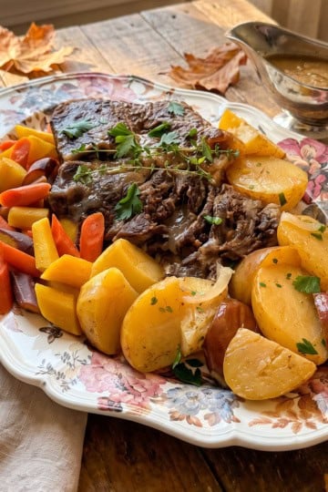 Roast beef pot roast with root vegetables and cider braised gravy resting on a wooden table.