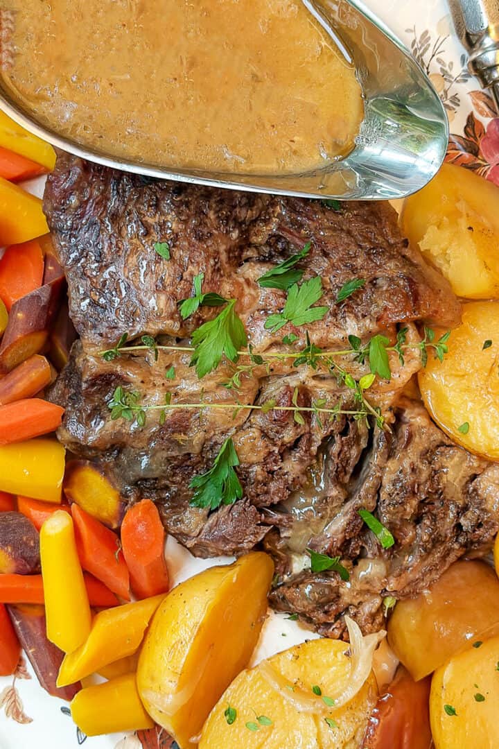 Apple Cider braised pot roast resting on a serving platter with tender potatoes and carrots ready for serving.
