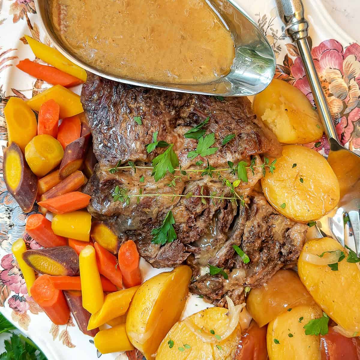 Apple Cider braised pot roast resting on a serving platter with tender potatoes and carrots ready for serving.