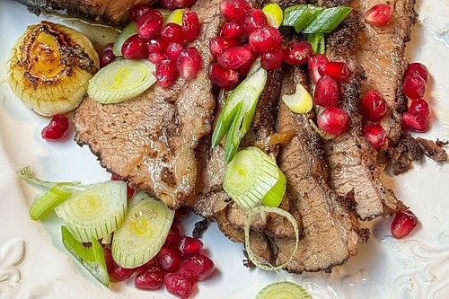 A plate of slow-cooked beef brisket served with pomegranate seeds, green onions, and roasted onions. The brisket is sliced and garnished, showcasing a rich, juicy texture. Perfect for your next brisket recipe adventure! "Slow Cooker Beef Brisket" text overlays the image.