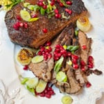 Square image of sliced slow cooker beef brisket on a white serving platter with pomegranate seeds.