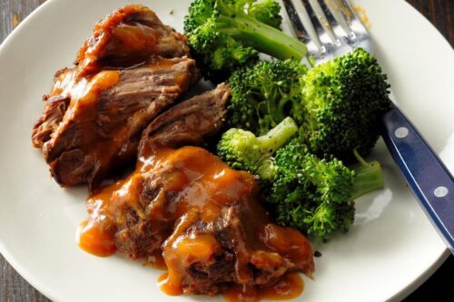 A plate of tender meat drizzled with sauce next to steamed broccoli, with a fork resting on the side.