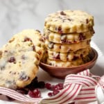 Stack of Cranberry Pistachio Shortbread Cookies on a white stand with red and white striped ribbon and dried cranberries on the plate.