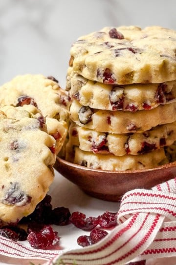 Stack of Cranberry Pistachio Shortbread Cookies on a white stand with red and white striped ribbon and dried cranberries on the plate.