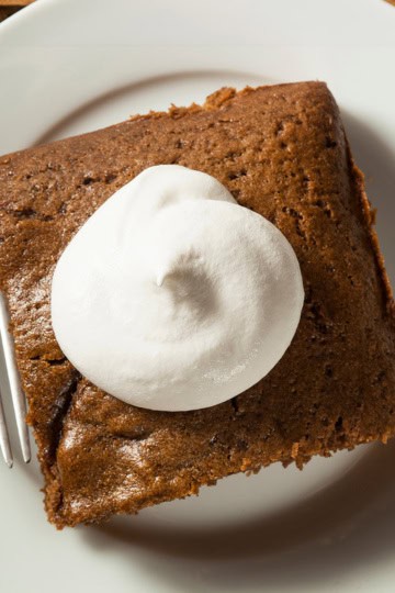 Top view of a gingerbread cake serving topped with whipped cream on a plate with a fork.