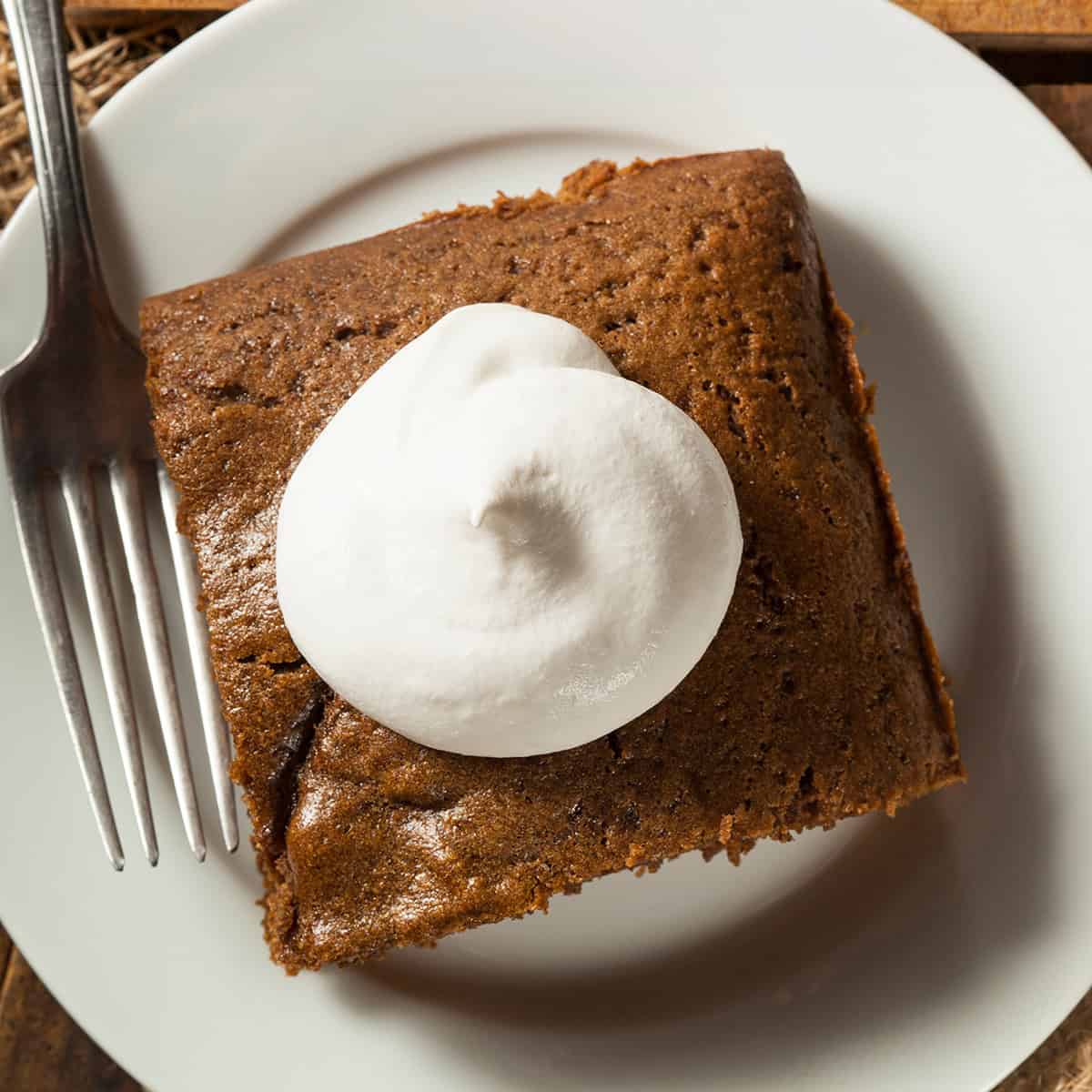 Top view of a gingerbread cake serving topped with whipped cream on a plate with a fork.