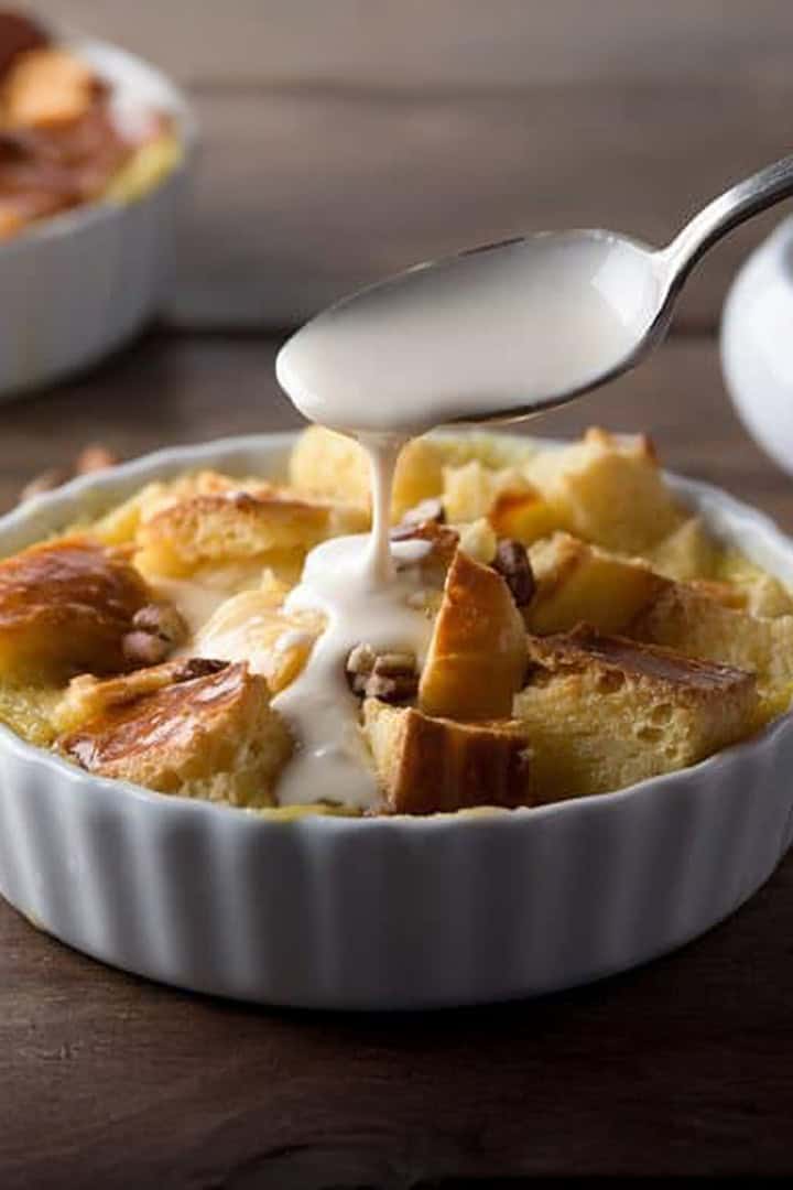 Single serving of brioche bread pudding in a individual tart shell with a spoon drizzling cream sauce over the top.