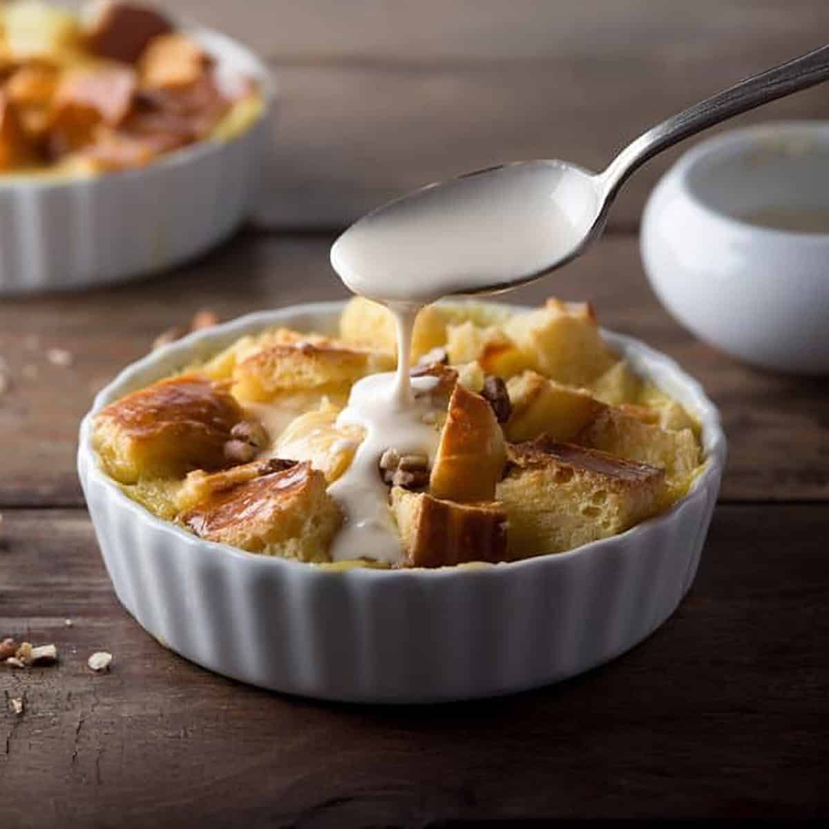 Single serving of brioche bread pudding in a individual tart shell with a spoon drizzling cream sauce over the top.