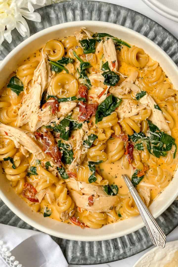 Marry Me Chicken Soup in a serving dish with a silver spoon with spinach, shredded chicken, and sun dried tomatoes.