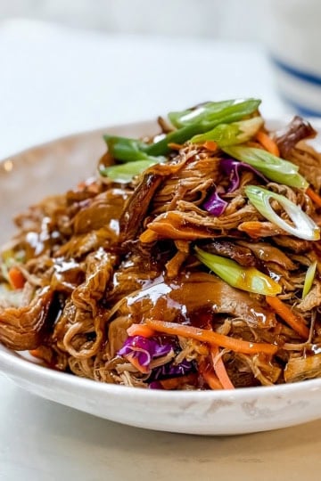 Crockpot Asian shredded pork in a bowl stopped with diagonally sliced scallions.