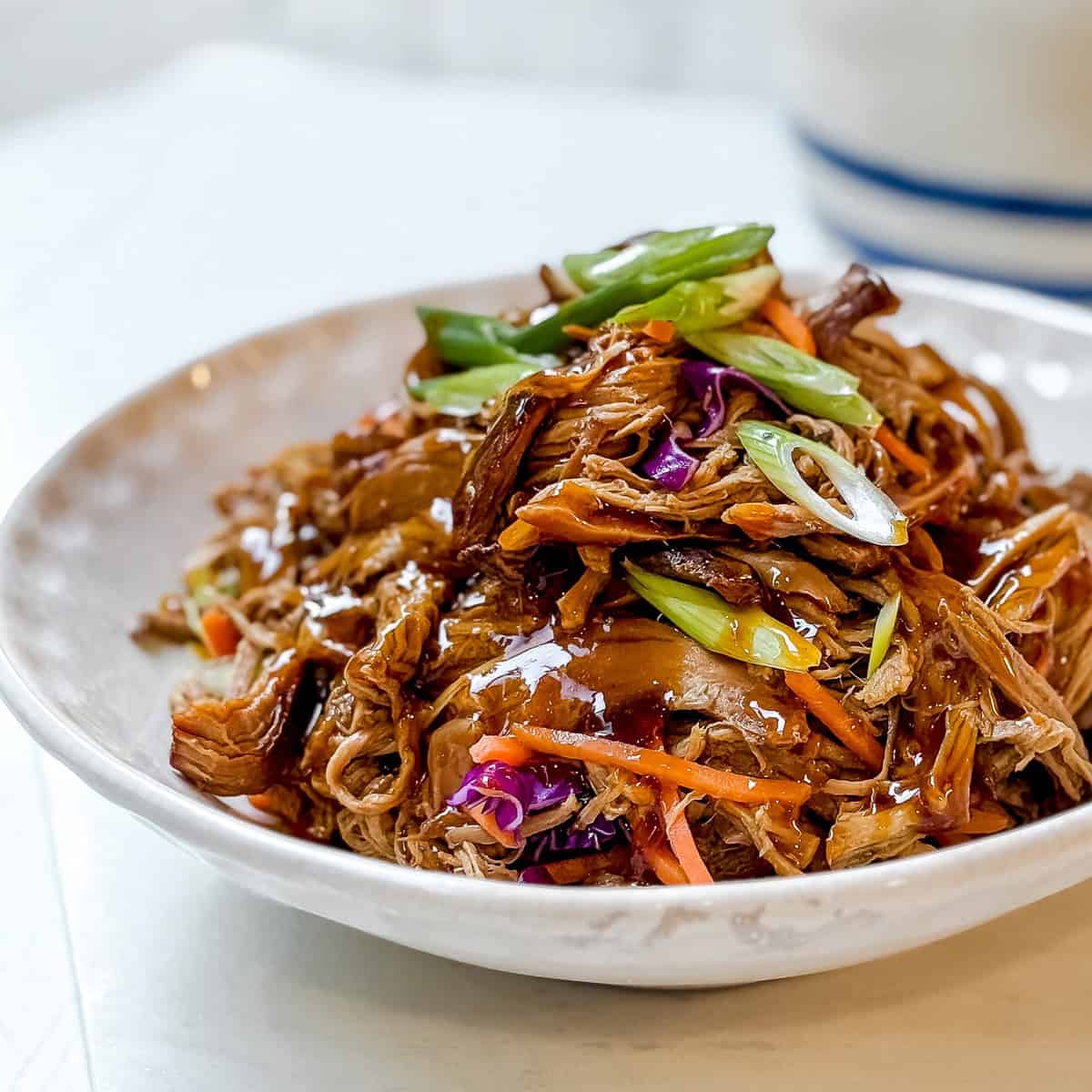 Crockpot Asian shredded pork in a bowl stopped with diagonally sliced scallions.