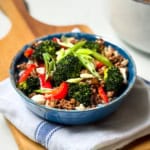 A blue bowl filled with savory Beef and Broccoli, red bell peppers, and sliced green onions served over white rice, placed on a folded white and blue cloth napkin.