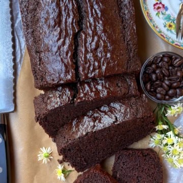 Partially sliced chocolate loaf cake on parchment paper with a serrated knife nearby.
