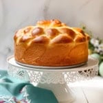 Side view of unsliced Easter Paska yeasted bread on a white spring stand with Easter eggs in the background.