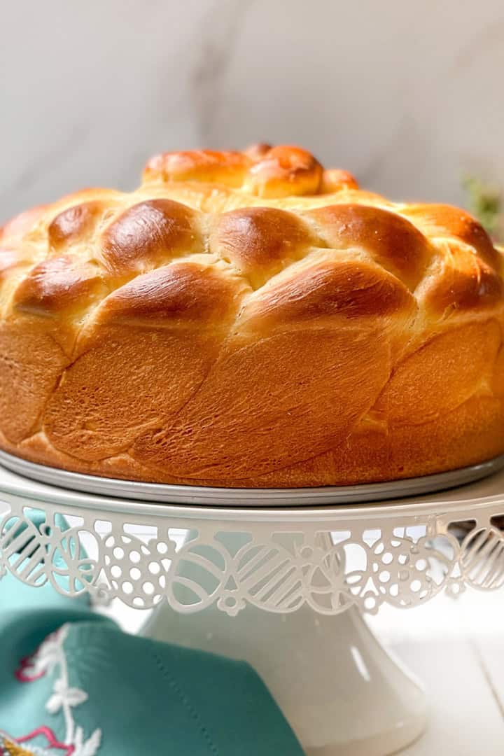 Side view of unsliced Easter Paska yeasted bread on a white spring stand with Easter eggs in the background.