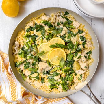 A pan of lemon chicken orzo, garnished with fresh herbs and slices of lemon.