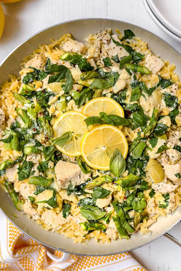 A pan of lemon chicken orzo, garnished with fresh herbs and slices of lemon.
