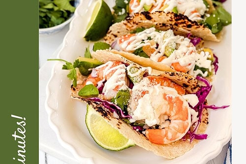A platter of shrimp tacos topped with lime crema sauce, red cabbage, and cilantro, garnished with lime wedges. Text reads: "31 Easy Shrimp Tacos with Lime Crema Sauce. Ready in minutes!.