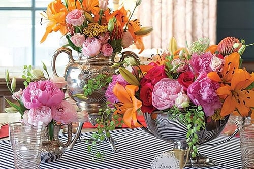 A Kentucky Derby party table is set with gold-rimmed plates, pink napkins, striped table runner, and elegant silver vases filled with vibrant blooms. Text overlay reads: "Kentucky Derby Party Ideas, decor, food & party tips!.