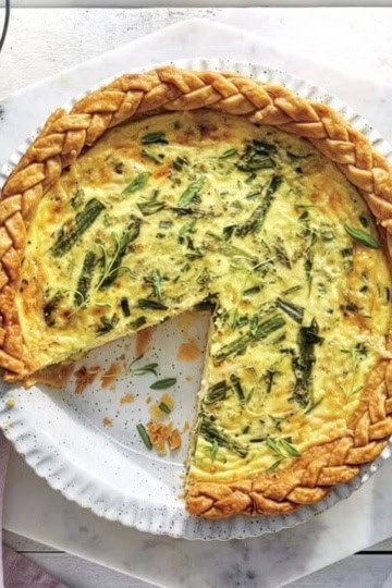 A baked quiche with a braided crust sits on a white plate, one slice removed—perfect for Easter Brunch.