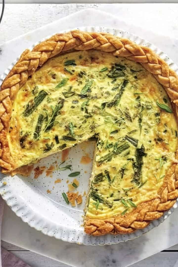 A baked quiche with a braided crust sits on a white plate, one slice removed—perfect for Easter Brunch.