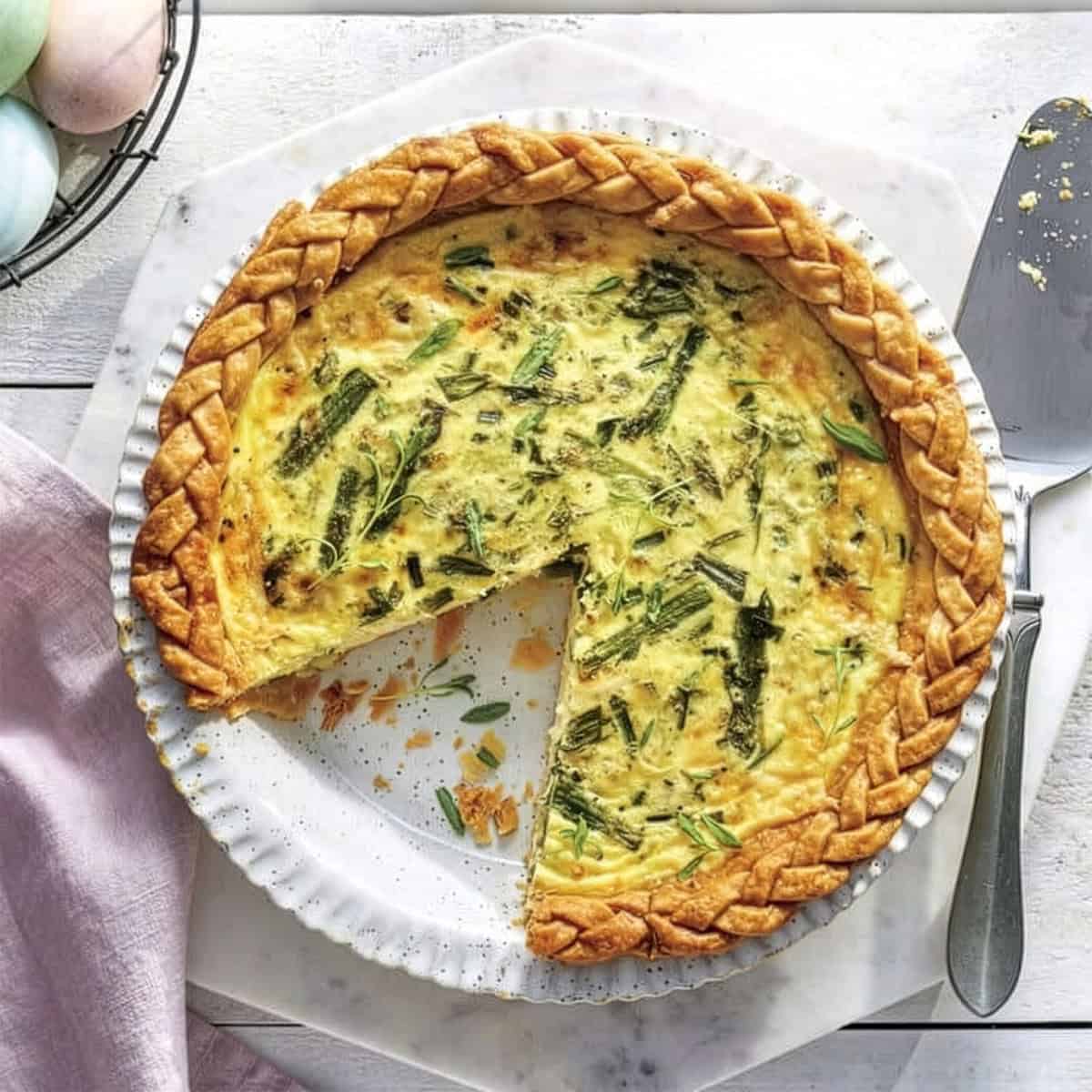 A baked quiche with a braided crust sits on a white plate, one slice removed—perfect for Easter Brunch.