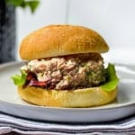 A tuna salad sandwich with lettuce on a round bun, served on a white plate—also great with ham salad for a tasty twist.