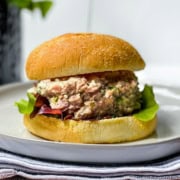 A tuna salad sandwich with lettuce on a round bun, served on a white plate-also great with ham salad for a tasty twist.