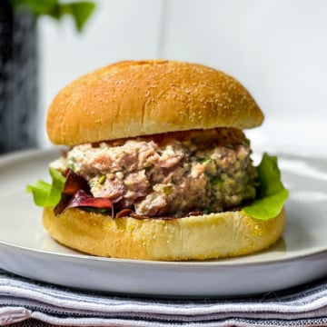 A tuna salad sandwich with lettuce on a round bun, served on a white plate-also great with ham salad for a tasty twist.