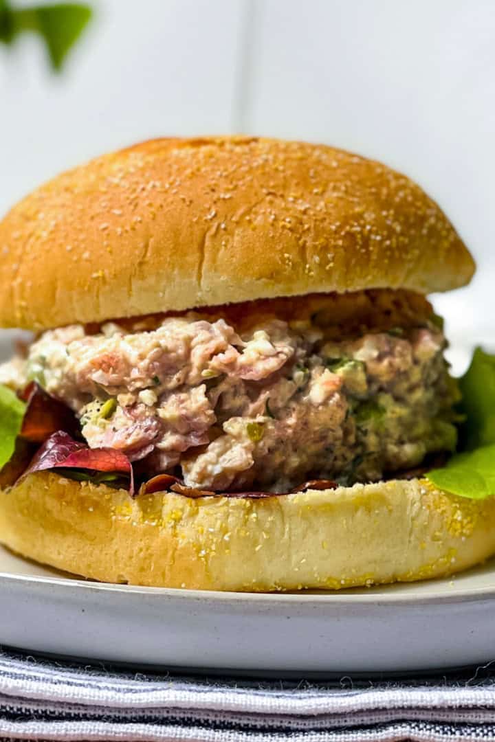 A tuna salad sandwich with lettuce on a round bun, served on a white plate-also great with ham salad for a tasty twist.