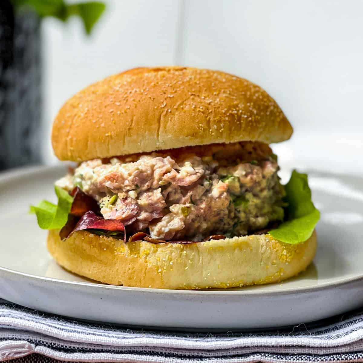 A tuna salad sandwich with lettuce on a round bun, served on a white plate-also great with ham salad for a tasty twist.