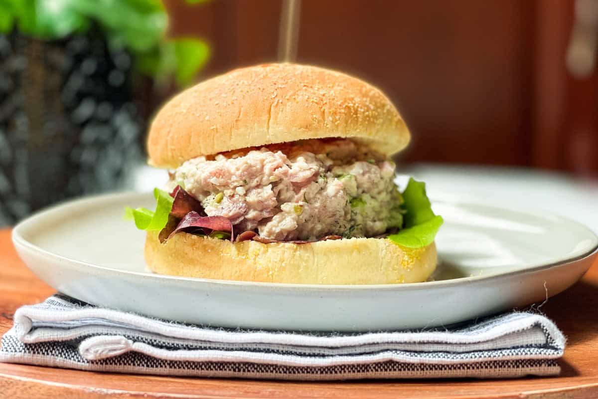 A ham salad sandwich with lettuce on a bun is served on a white plate with a napkin underneath.