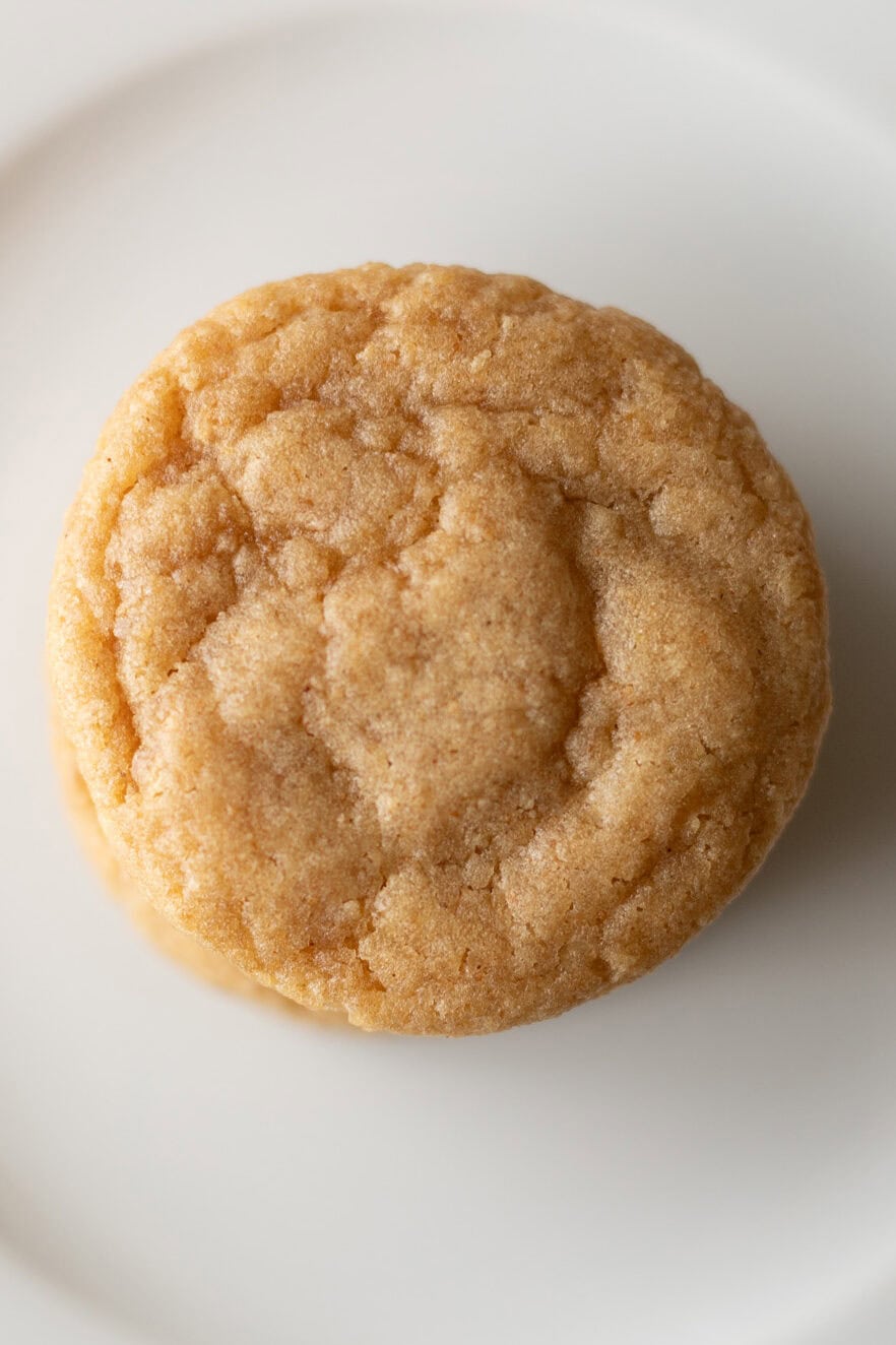 A single round graham cookie with a slightly cracked surface sits on a white plate seen from above.