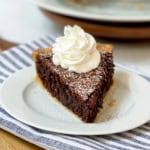 A slice of chocolate pie topped with whipped cream and powdered sugar on a white plate, set on a striped cloth—perfect for Father's Day dessert recipes.