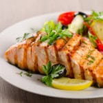 Honey glazed salmon fillet garnished with parsley and served with lemon slices, black olives, and a side salad of lettuce, tomato, and cucumber on a white plate.