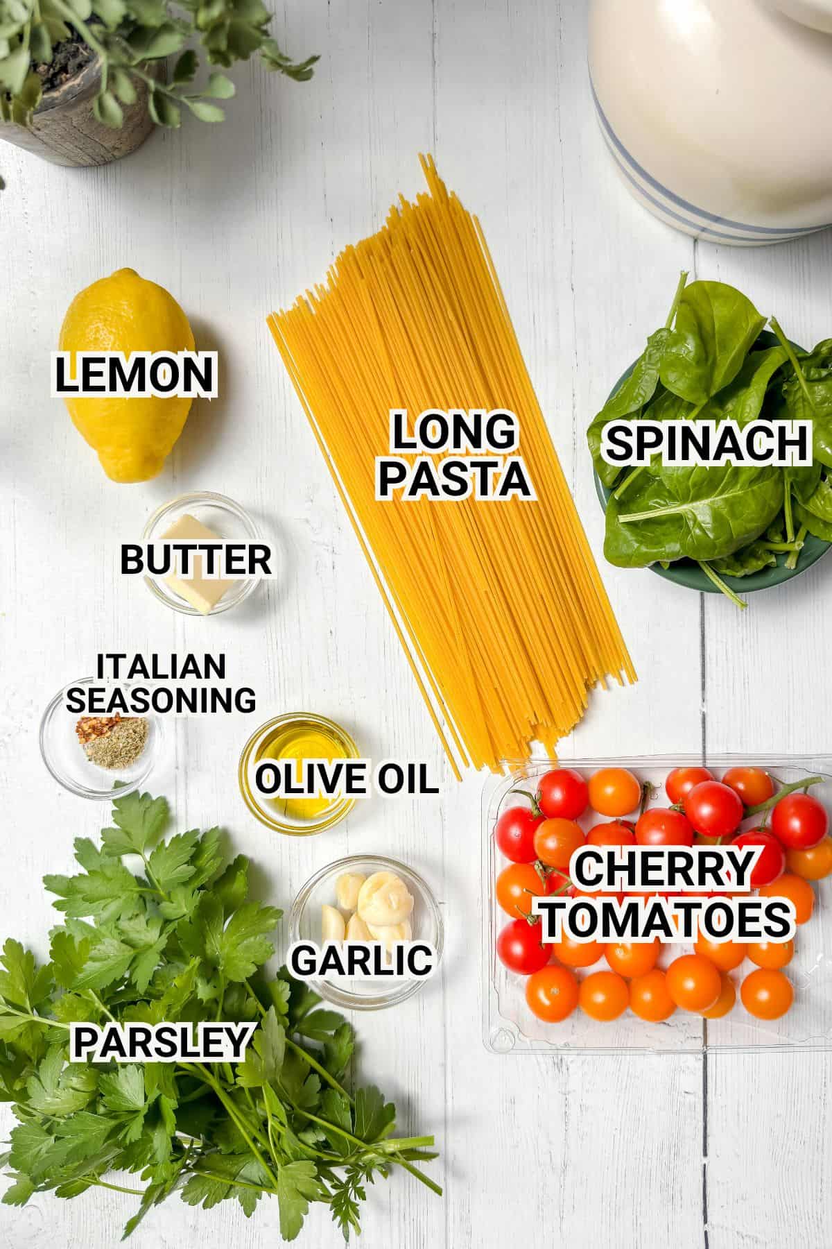 Ingredients for a pasta dish are arranged on a white surface: long pasta, spinach, cherry tomatoes, lemon, butter, parsley, garlic, olive oil, and Italian seasoning, each labeled with text overlays.