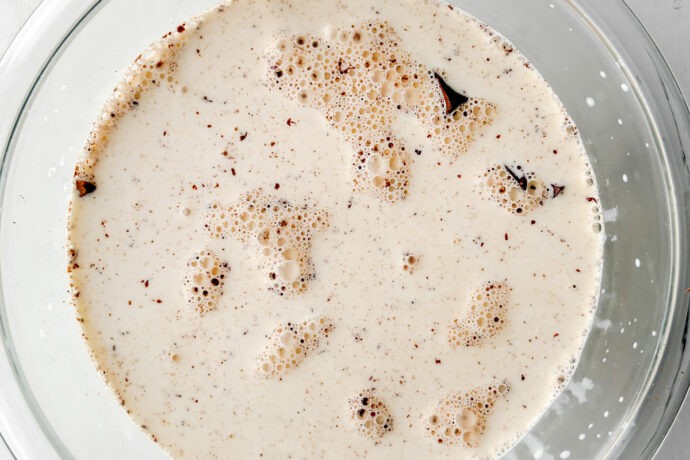 A glass bowl filled with a creamy mixture—speckled and bubbling—sits on a white wooden surface, ready to become the luscious base for a no-bake s'mores icebox cake.