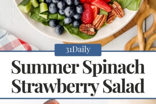 A vibrant spinach strawberry salad in a white bowl is topped with raspberries, blueberries, diced cucumbers, pecans, feta cheese, and red bell peppers, shown from above and served with a wooden spoon.