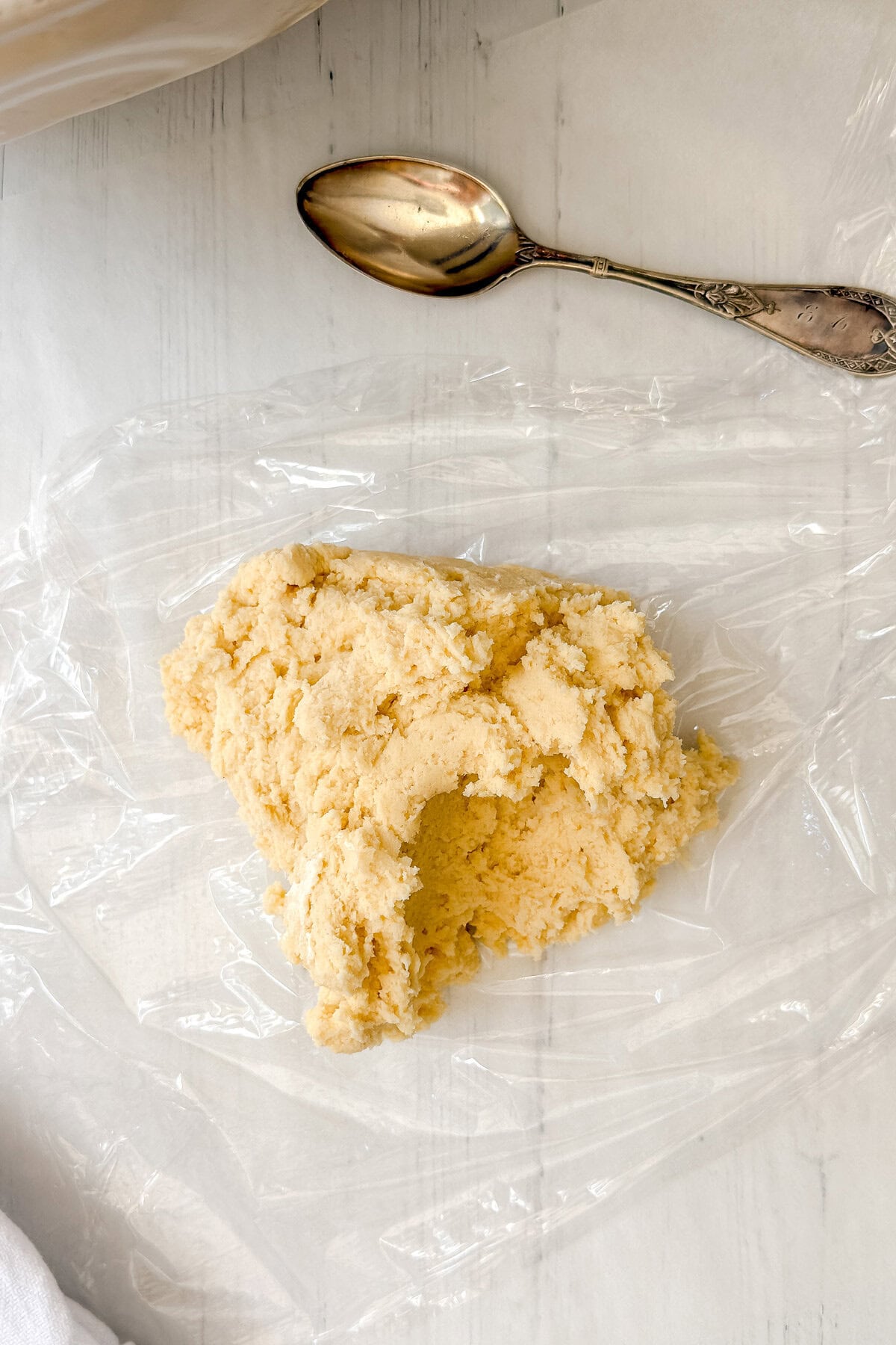A mound of pale dough rests on a sheet of clear plastic wrap on a white surface, with a silver spoon placed nearby-ready to be shaped into homemade treats reminiscent of classic Girl Scout Cookies.