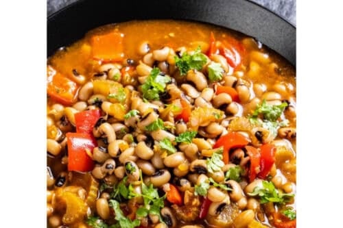 A bowl of Ikarian stew with black-eyed peas, chopped vegetables, and herbs in a tomato-based broth, garnished with fresh parsley. Text reads: “Easy Ikaria Stew. Blue Zone Longevity Recipe.”.