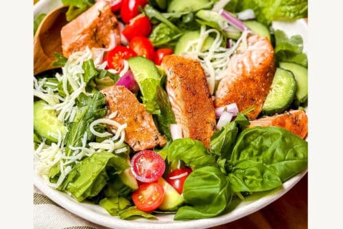A bowl of fresh salmon salad with lettuce, cherry tomatoes, cucumber, red onion, and citrus dressing, garnished with greens. Text reads: "Easy Salmon Salad with Citrus Dressing. Get the secrets!.