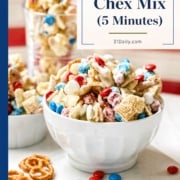 A white bowl of 4th of July Chex Mix with red, white, and blue candies, pretzels, and a glass of more mix in the background, set on a table with a patriotic theme.
