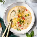 Bowl of Corn Chowder with garnishes or herbs and fresh corn with two spoons in the bowl.