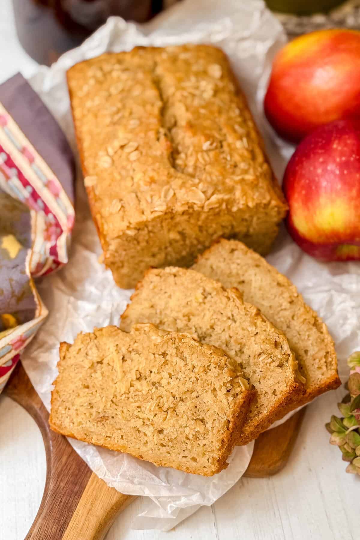 A loaf of apple oatmeal bread with three slices cut, placed on parchment paper.