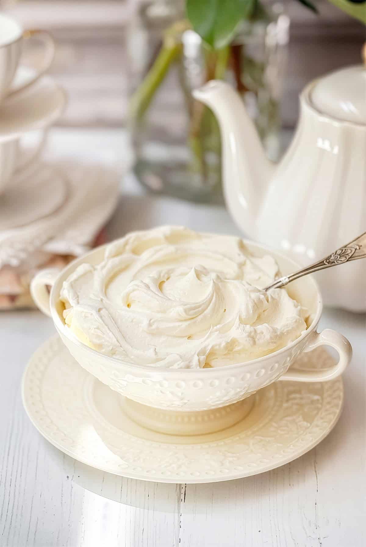 A bowl of homemade mock clotted cream with a spoon placed on a matching saucer.