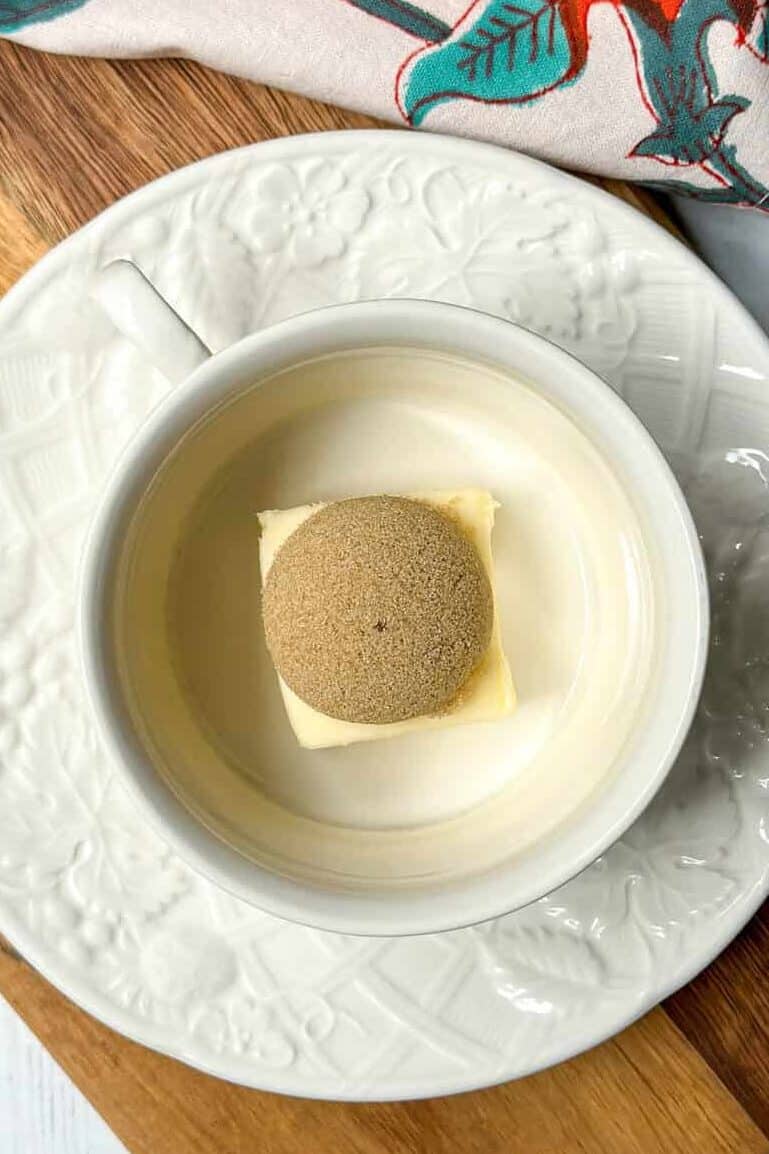 A bowl of water and a spoon on a wooden cutting board.