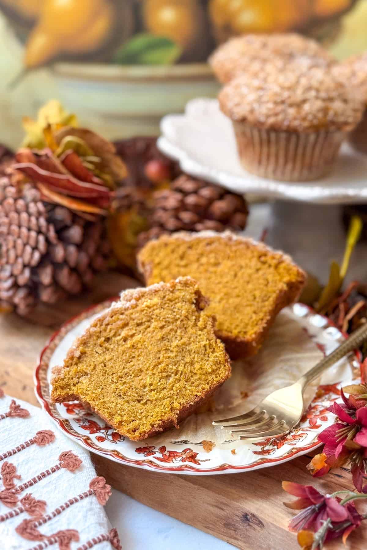 Two halves of a Pumpkin Muffin sit on a decorative plate with a fork.