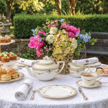 A lace-covered table set for tea with floral china, a teapot, cups, a tiered tray for a September afternoon tea.