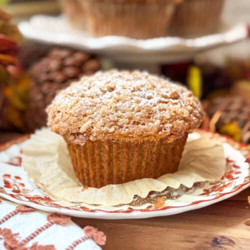 A crumb-topped Panera Pumpkin Muffin dusted with powdered sugar sits on a decorative plate.